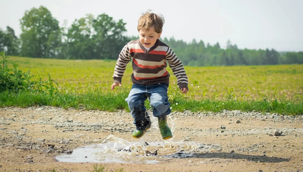 young boy in boots jumping over puddle